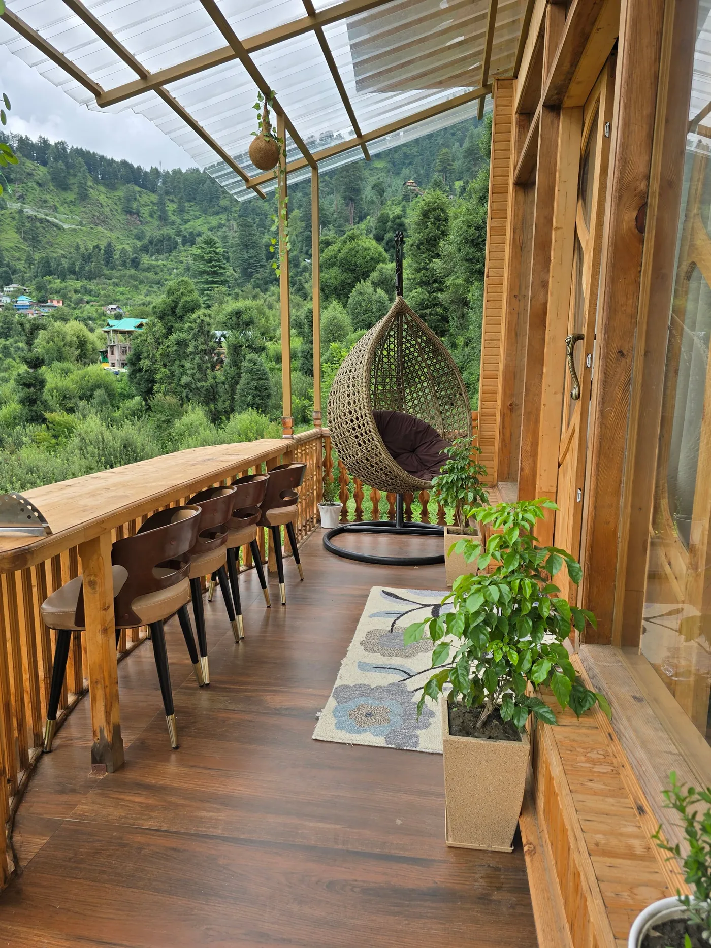 Deck with a hanging egg chair looking over forested slopes near Kasol