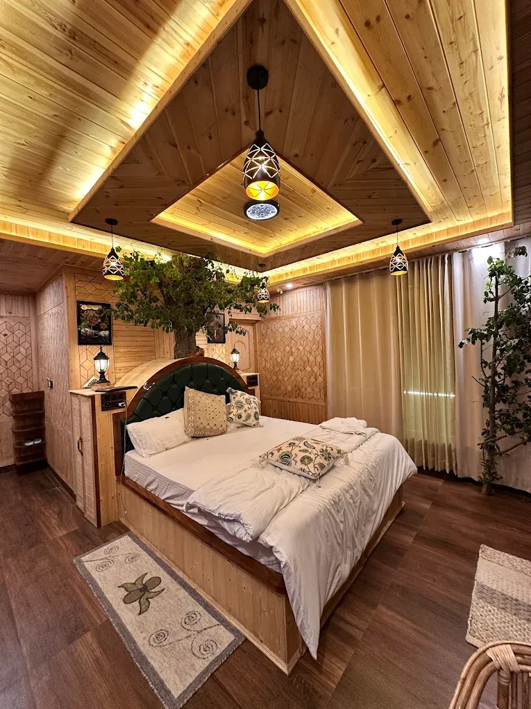 Wide view of the Deluxe Room with warm cove lighting, lanterns and a tree beside the bed