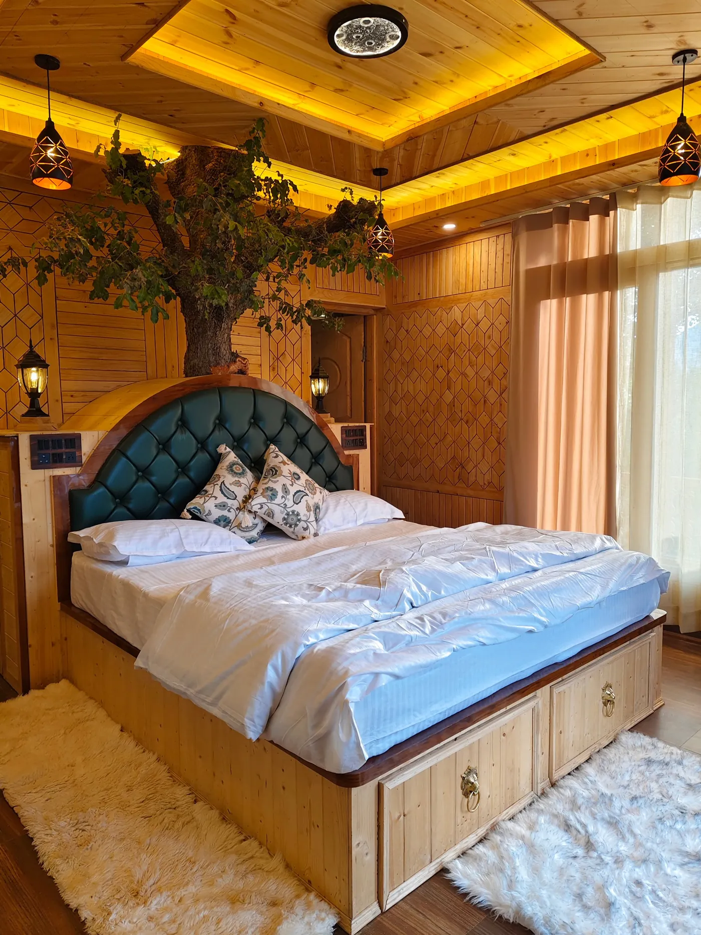 Deluxe Room at Shree Tree House near Kasol with a king bed, tufted green headboard, a tree beside it and a glowing timber ceiling