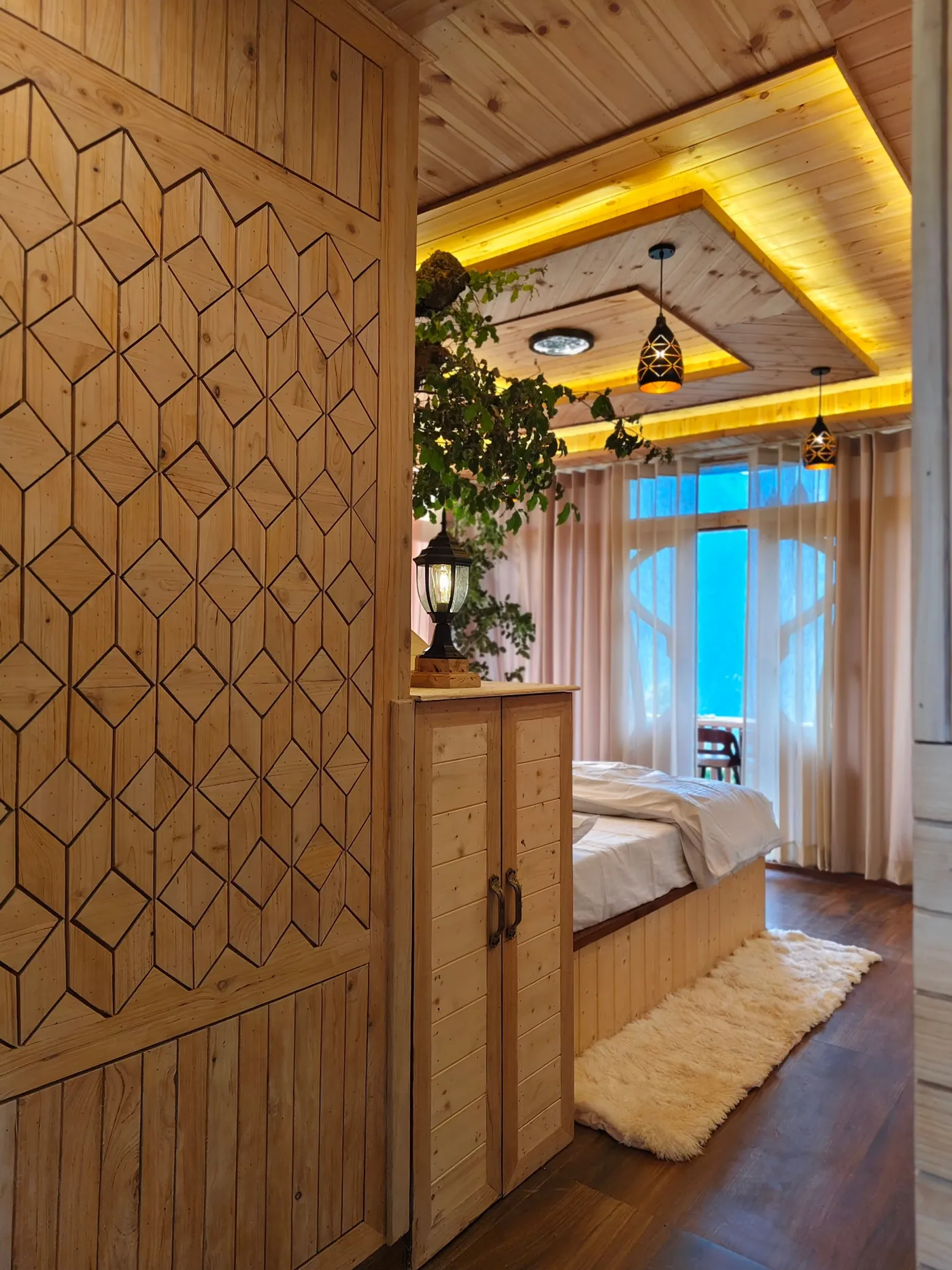 Carved geometric timber panel at the entrance of the Deluxe Room with the bed and balcony door beyond