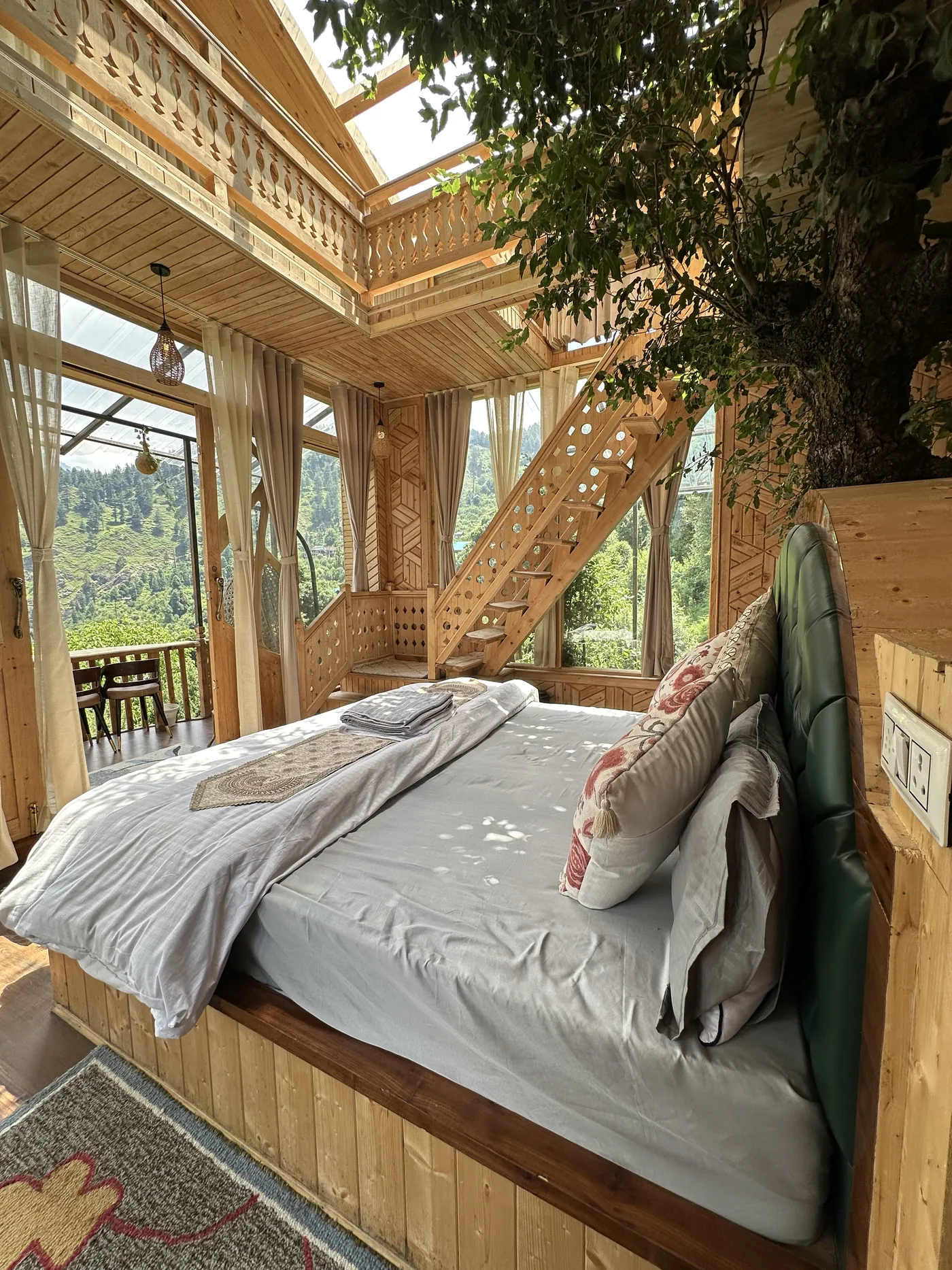 King bed in the Duplex Tree House beside the carved staircase, with the forest visible through glass