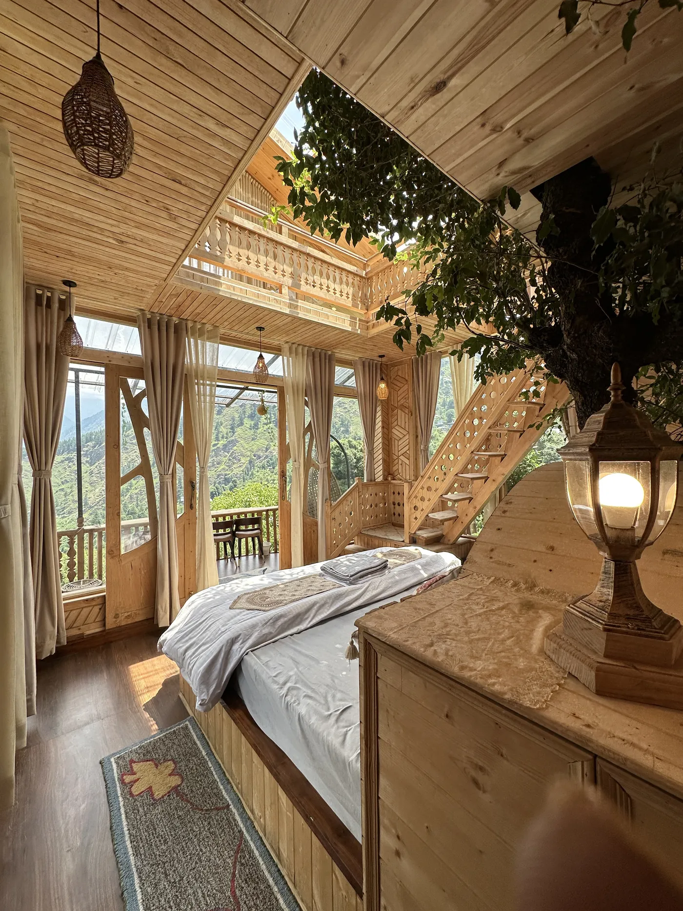 Inside the Duplex Tree House at Shree Tree House: a lantern, the carved staircase and a tree rising through the room