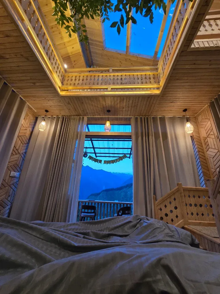 Looking up from the bed in the Duplex Tree House through the double-height space to the loft balustrade, the skylight and the mountains at dusk