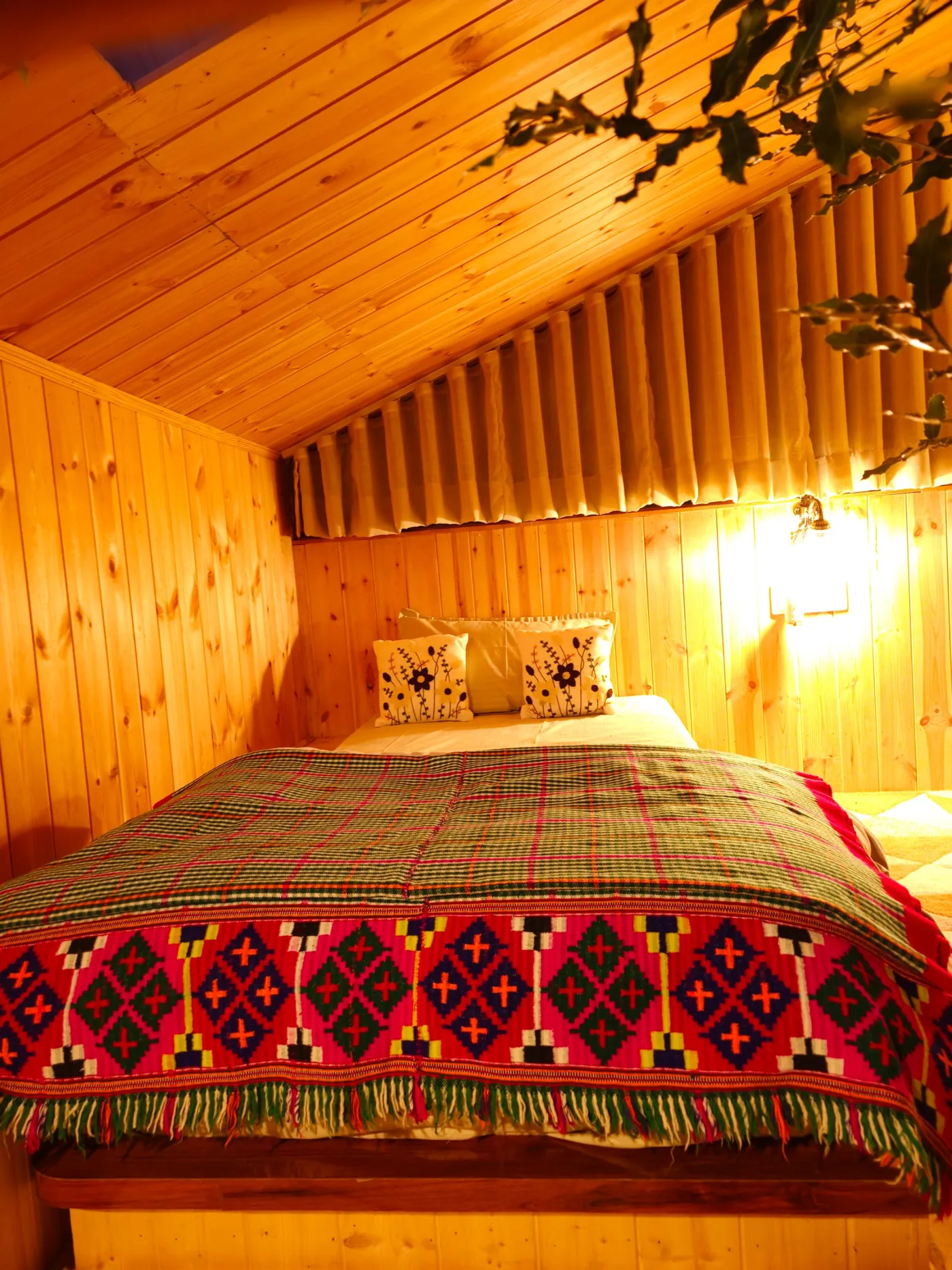 Single bed in the loft with a Himachali blanket under the sloping pine roof