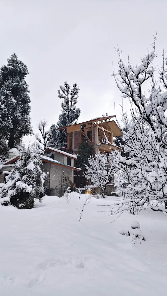 The timber frame of the third stay rising behind the existing building, with fresh snow on the trees and the ground